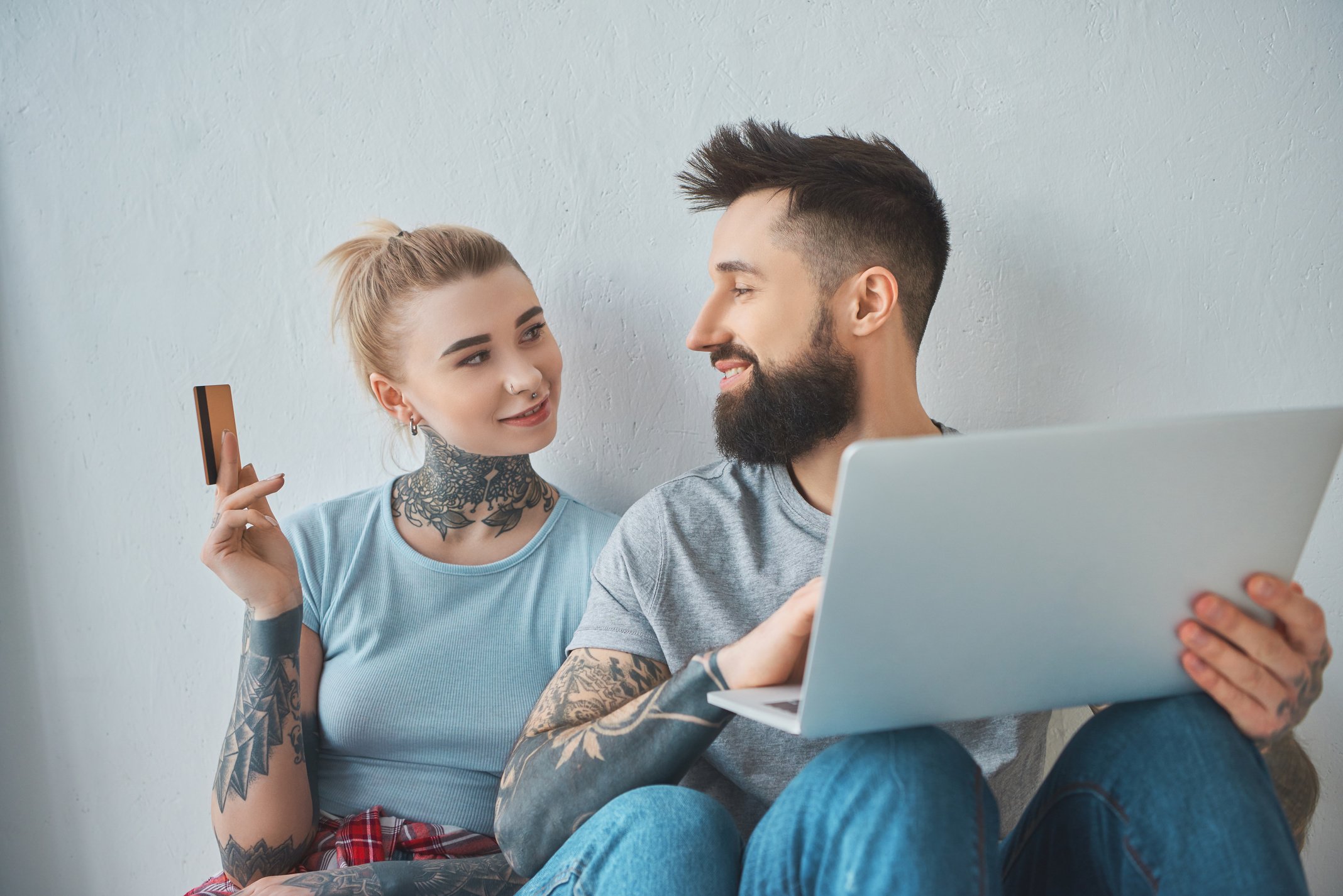 portrait of tattooed couple with laptop and credit card shopping online at new apartment